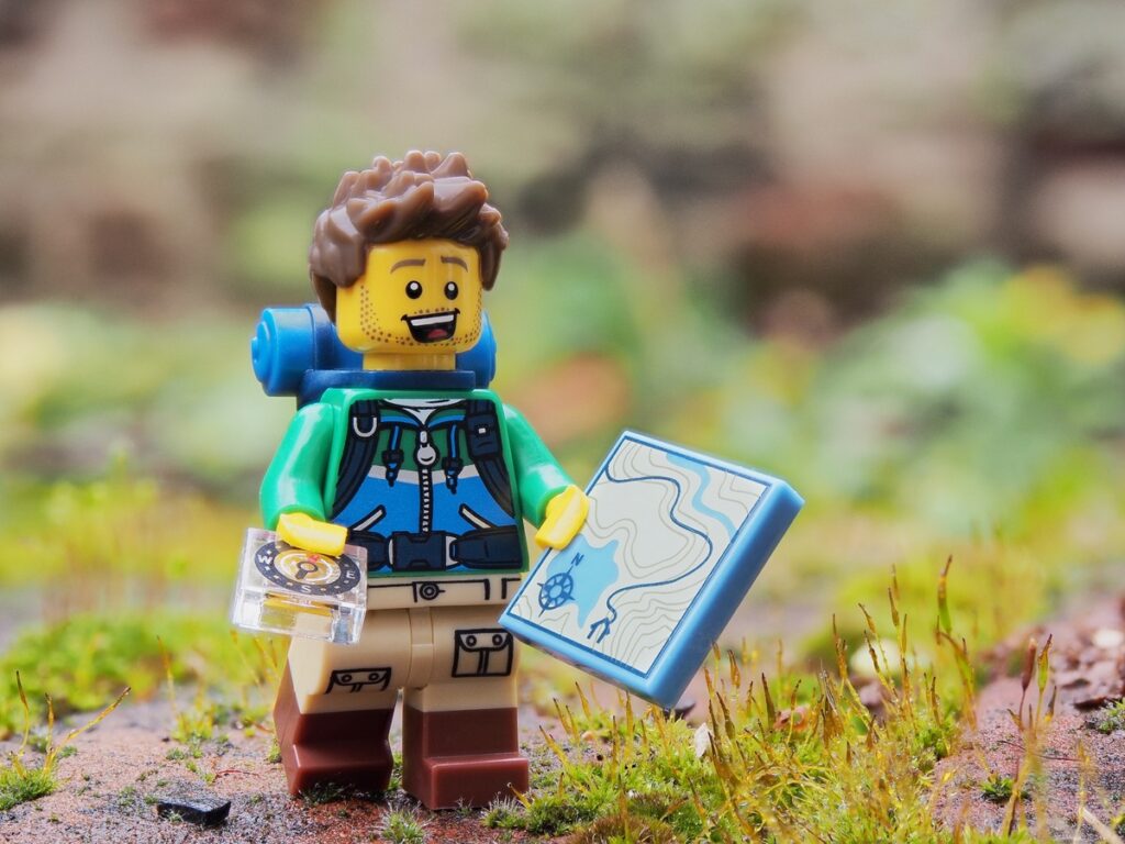 A Lego hiker, map and compass in hand, treks across a rocky landscape. This image symbolizes a startup strategically planning its course to success, using a strategy for startups.