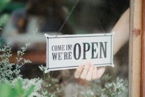 A slightly crooked "Open" sign hangs precariously in a shop window, reminding us that even small imperfections can be part of a charming small business strategy. The owner has a well developed small business strategy and is looking forward to the future confidently. Photo by Amina Filkins