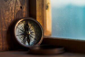 A close-up of a vintage compass resting on a wooden window sill. The compass is a symbol of direction and guidance, and it can serve as a metaphor for defining purpose in strategy. Photo by Jordan Madrid on Unsplash